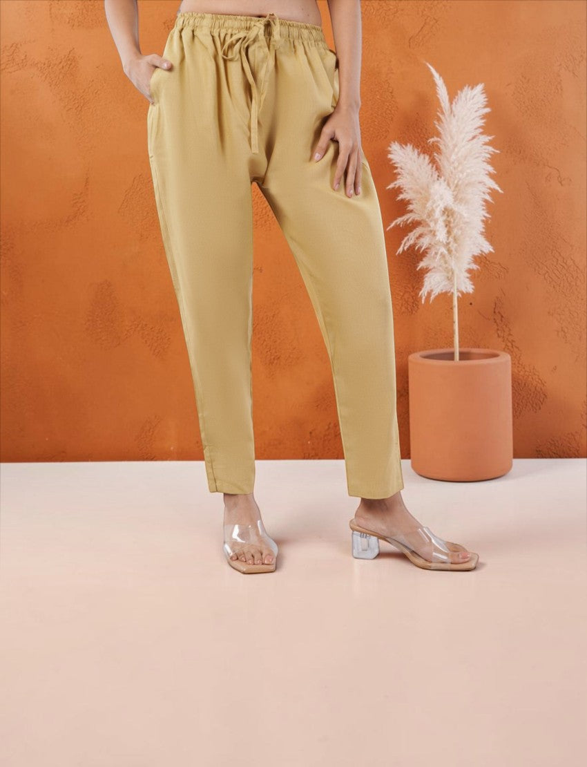 Eelika beige cotton trouser with an elasticated drawstring waist, worn with clear block-heeled sandals.