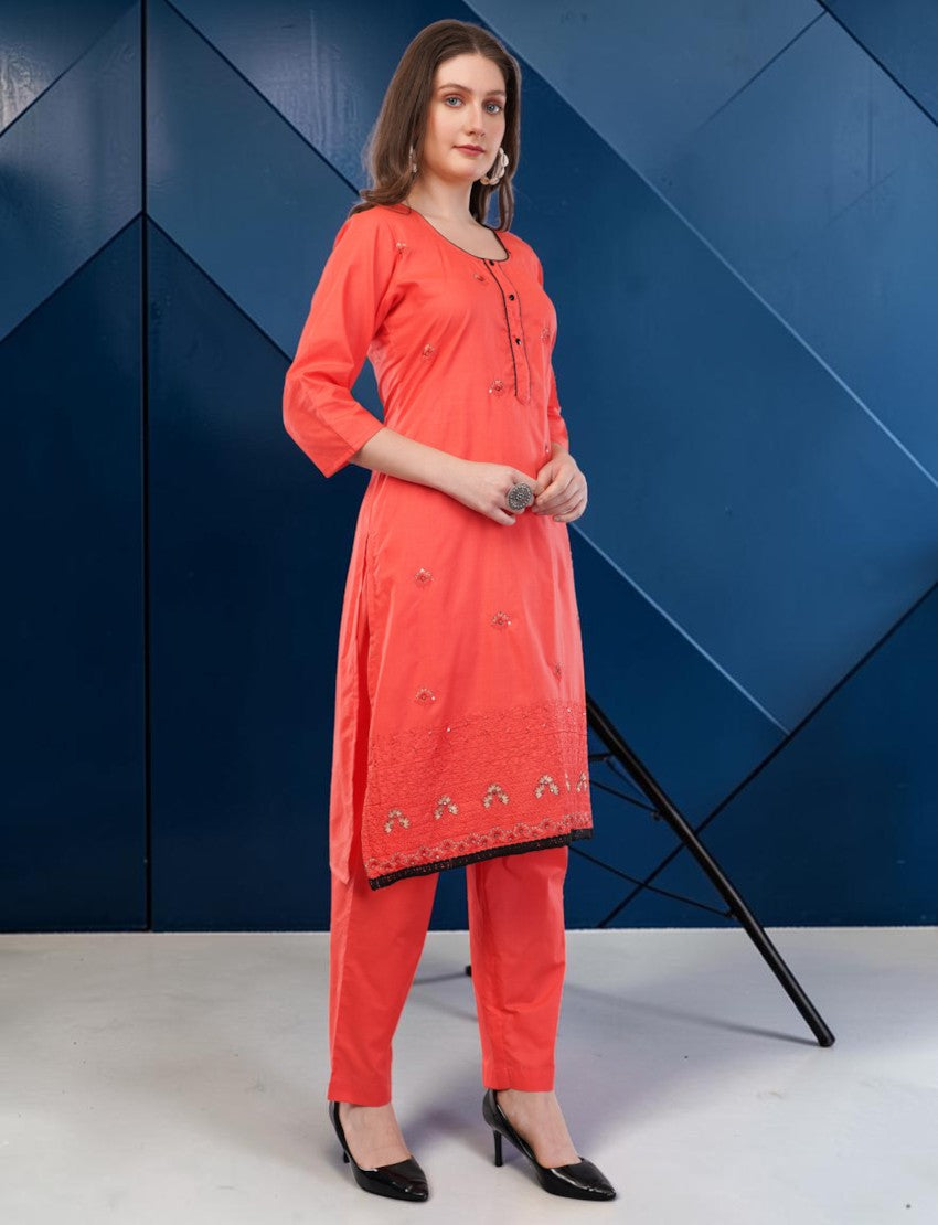 A woman wearing an Eelika coral red cotton salwar suit with 3/4 sleeves, embroidery, and a black lace border.