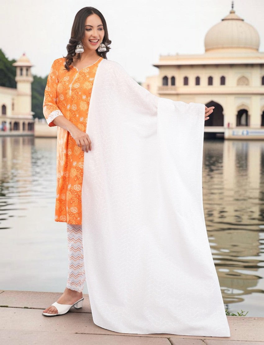 Eelika orange cotton salwar suit set with floral paisley print, V-neck, 3/4 sleeves, and white dupatta by water.